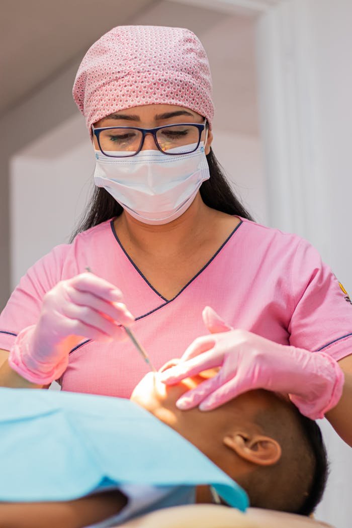 A dentist in pink uniform examining a patients teeth, focusing on dental care.
